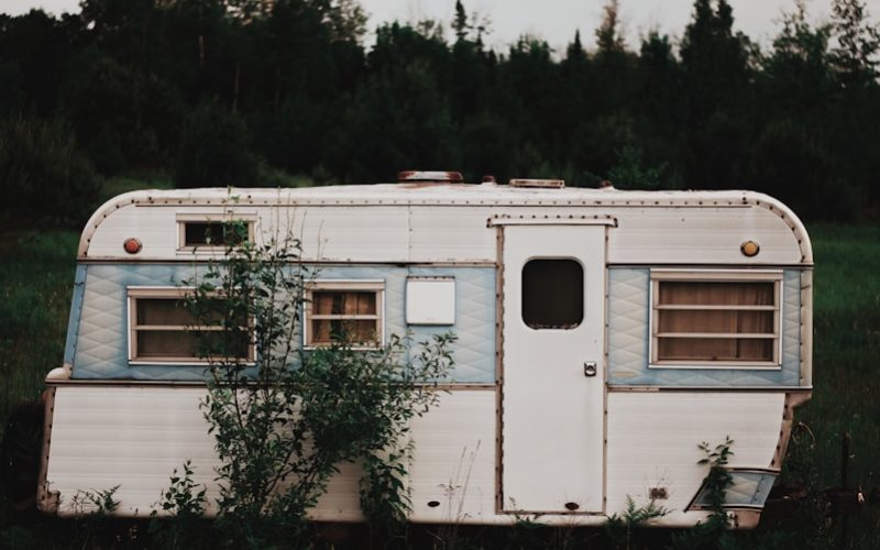 white RV trailer on grass field near trees under cloudy sky