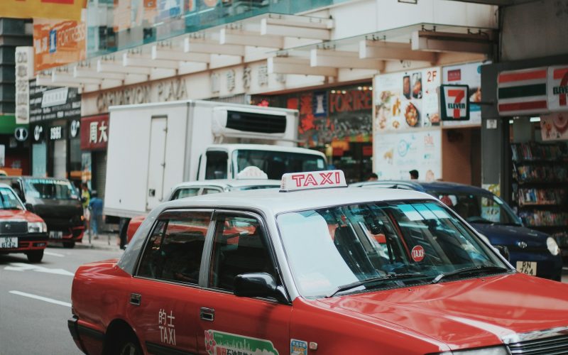 red and white taxi sedan running on road near 7 Eleven store signage